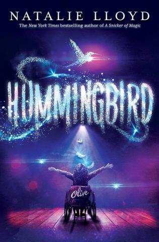 cover for "Hummingbird" book by Natalie Lloyd. Child in wheelchair, their arms stretched out towards a crowd. There's a spotlight on them. Pink and blue colors. Name "Olive" on the wheelchair. Hummingbird animal floating above title